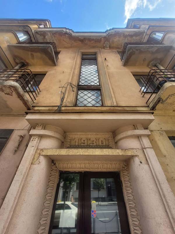 Tarpukario pastato fasadas, žiūrint iš apačios, su skaičiumi "1930" virš įėjimo.