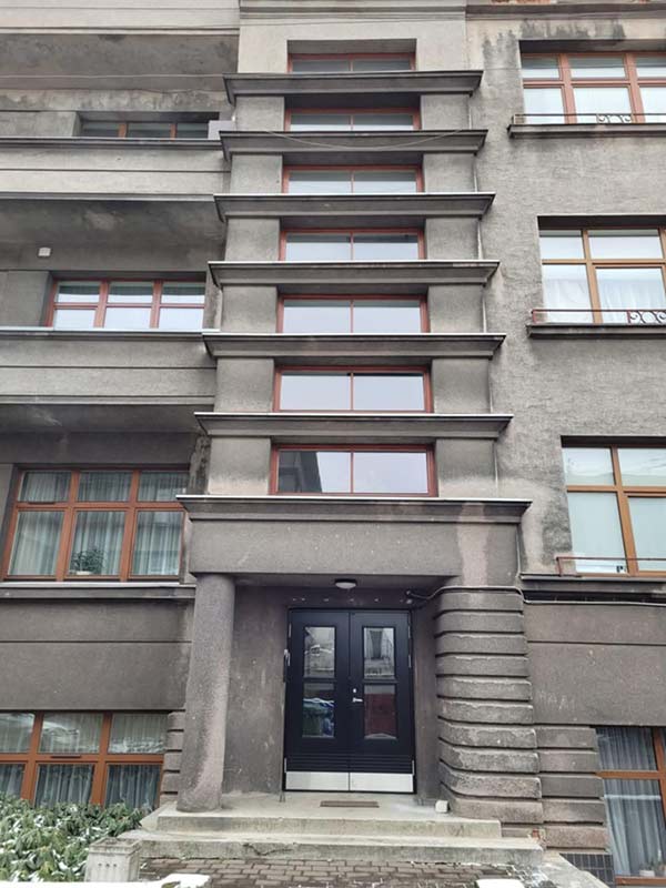 Pilkas, kelių aukštų pastatas su laiptuota fasado apdaila ir daugybe langų.